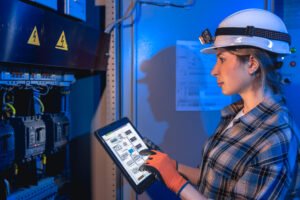 Woman electrician checks electrical panel using tablet. System control.